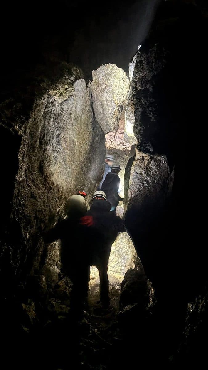Scouts exploring a narrow cave passage with helmet torches